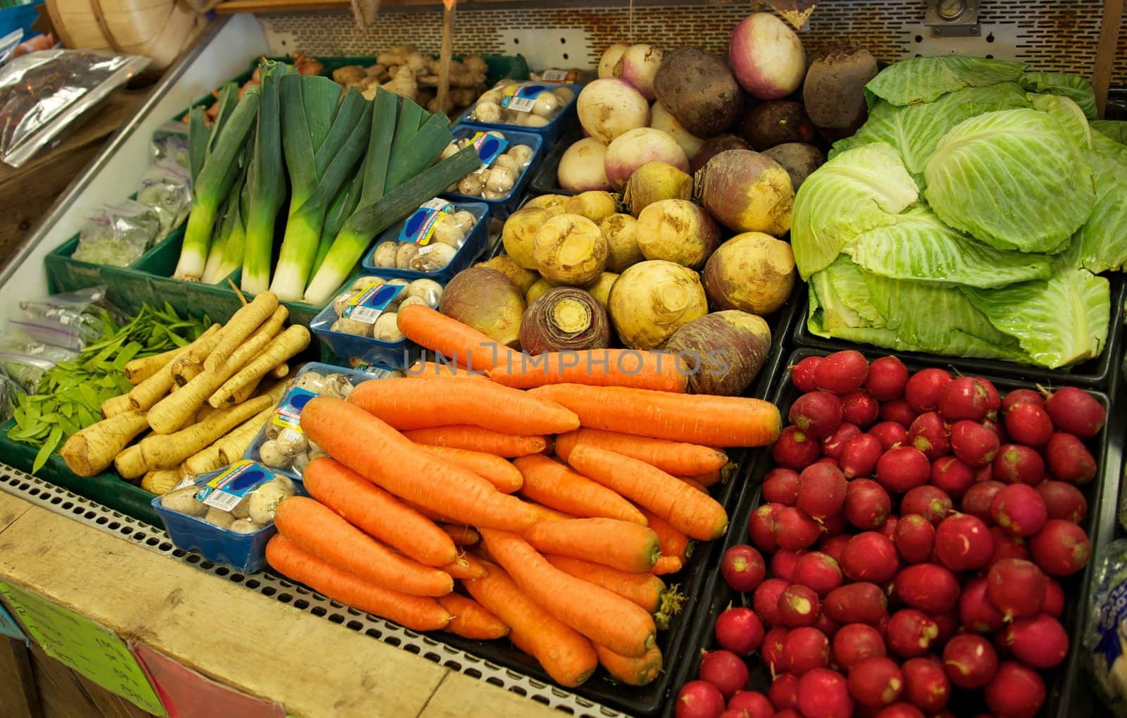 A vegetable bin full of onions, carrots, mushrooms, cabbage leafs, radishes and potatoes at a grocery store