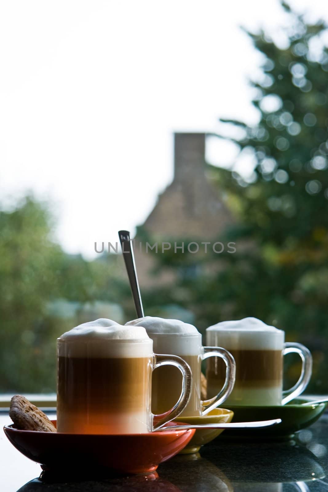 Black granite kitchen dresser with three glass mugs "cafe au lait", colorful saucers and view through window - vertical image