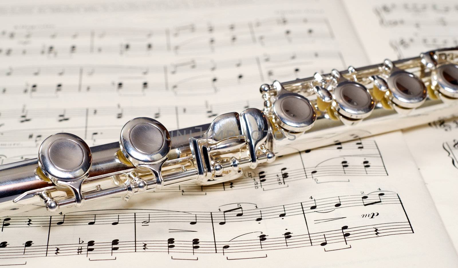 Closeup view of the keys of a metal flute, shot on a music sheet