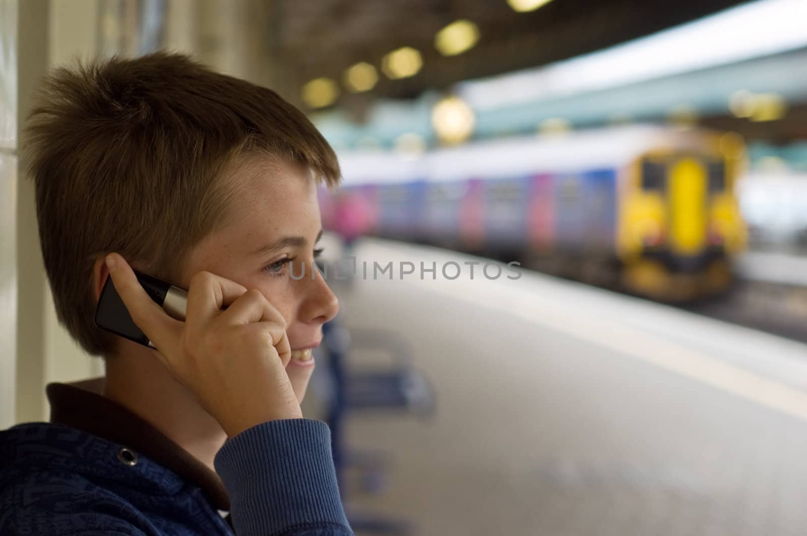 a teenage boy laughing and talking on a mobile phone at a train station.