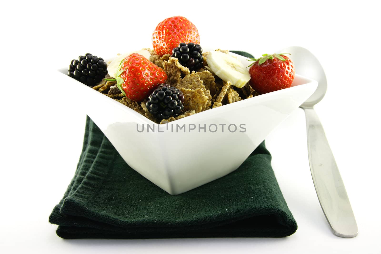 Crunchy delicious looking bran flakes and juicy fruit in a white bowl with a spoon and a black napkin on a white background