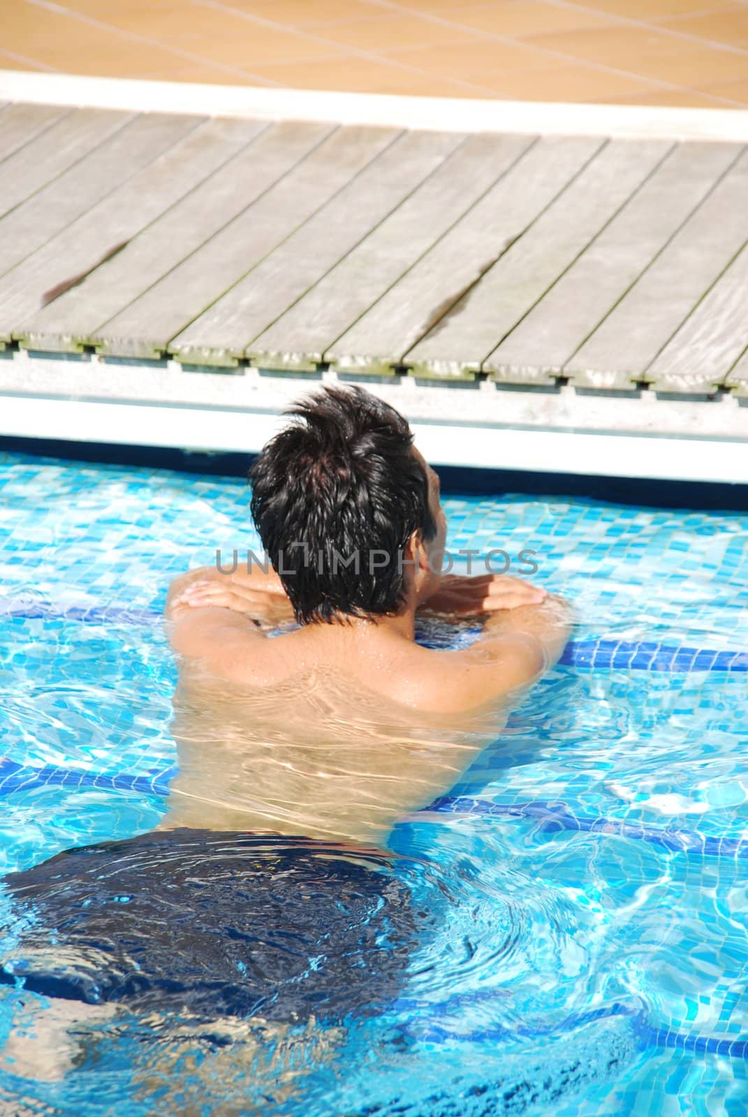 Young man relaxing at the edge of the swimming pool by luissantos84