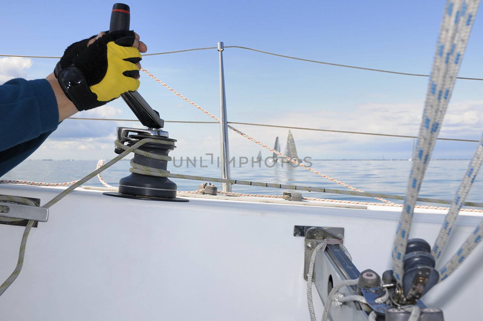 Hand holding a winch handle with sailboats in background