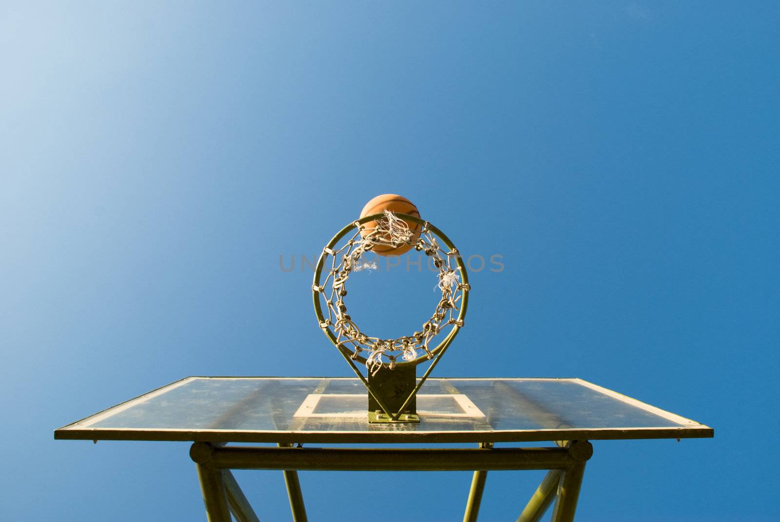 Basketball just before dropping into the net in a basketball game on an open court at sunset, seen directly under the net.