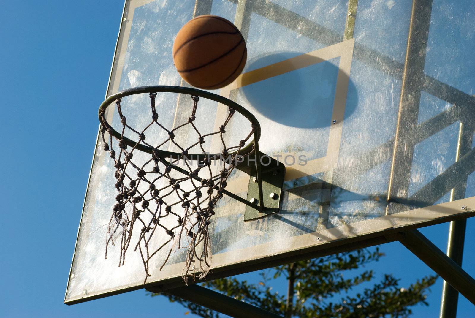 Basketball dropping into the net in a basketball game on an open court at sunset