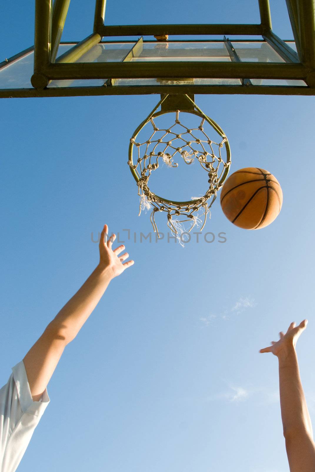 Boys challenging for the ball under the net in a casual game of basketball on an open court at sunset
