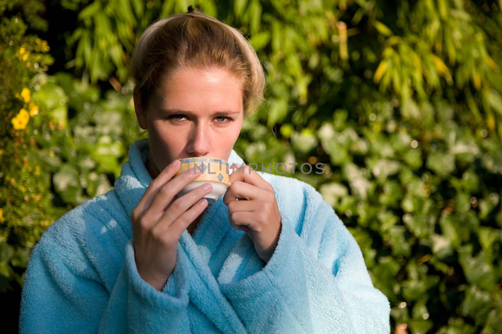Beautiful blond woman sitting in the early morning sunshine enjoying her coffee