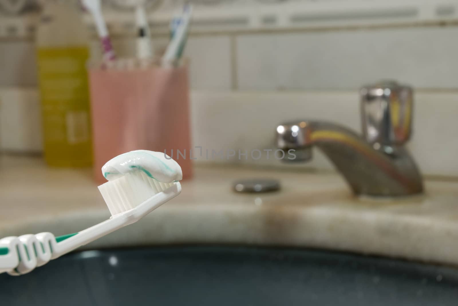 Detail shot of a tooth brush with tooth paste on it and basin in the blurred background