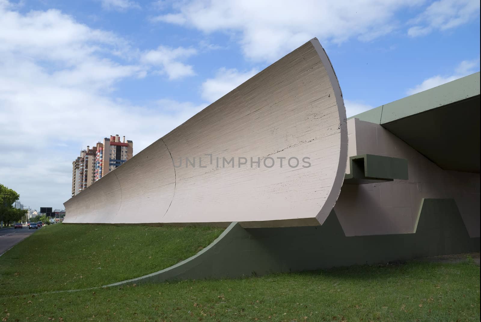 Wide angle shot of an architectural detail looking like half of a half-pipe. Blue sky and a couple of buildings in the background. Copy space in perspective.