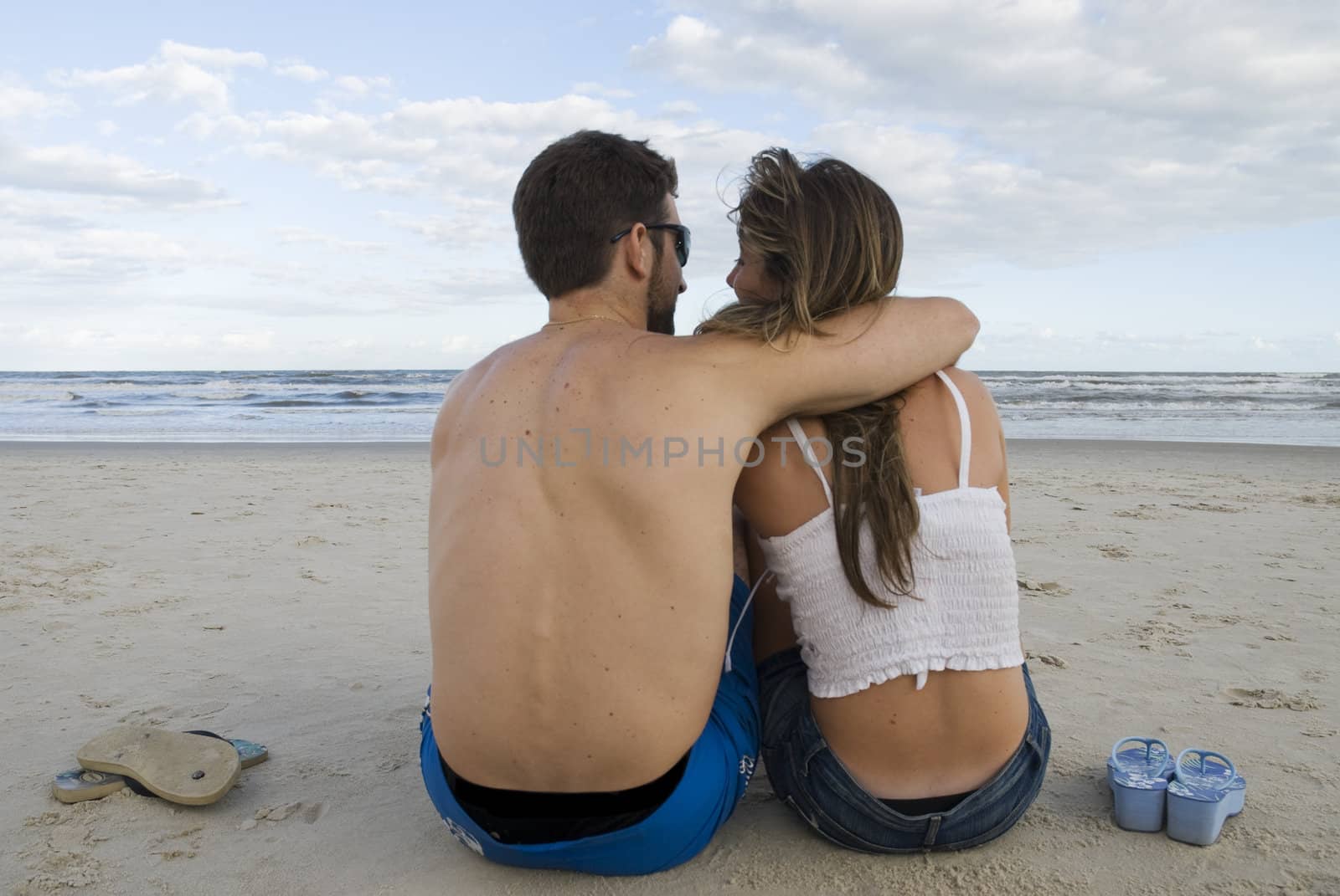 Young healthy couple sitted in the sand, looking out into the sea.