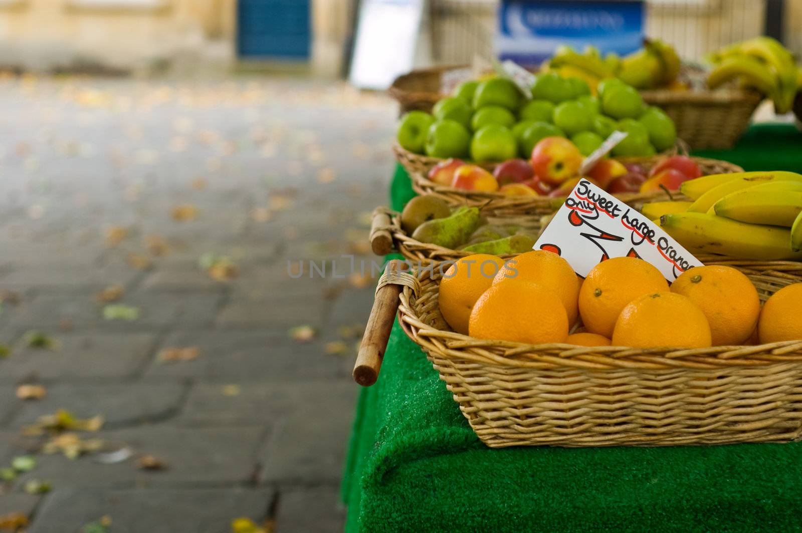 an autumn fruit and veg stall showing assorted fruits and autumn fall leaves on the blurred pavement 