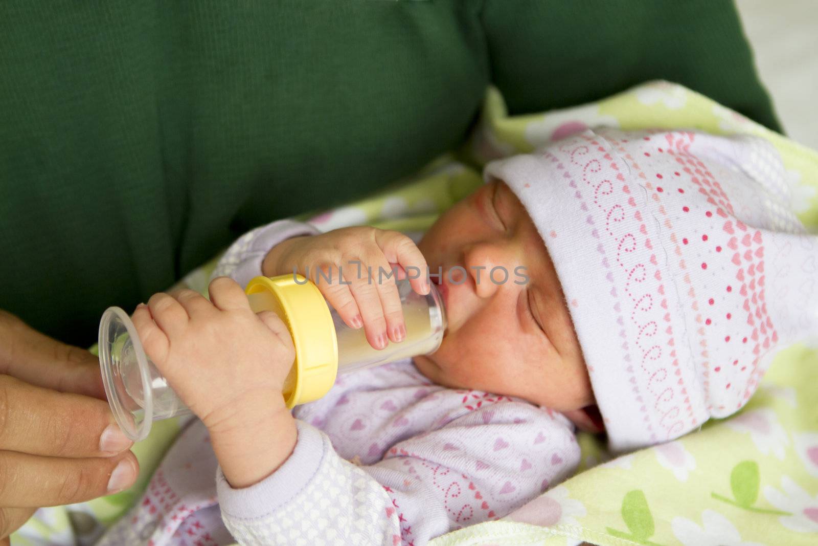 Couple days old baby holding on to her bottle while her eyes shut.