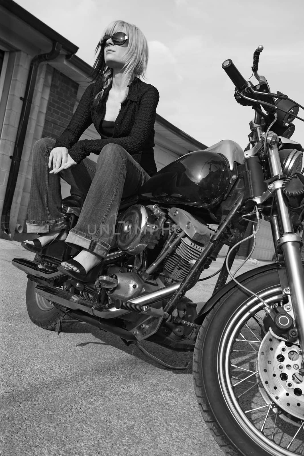 Black and white image of a beautiful blonde female sitting on a motorcycle.
