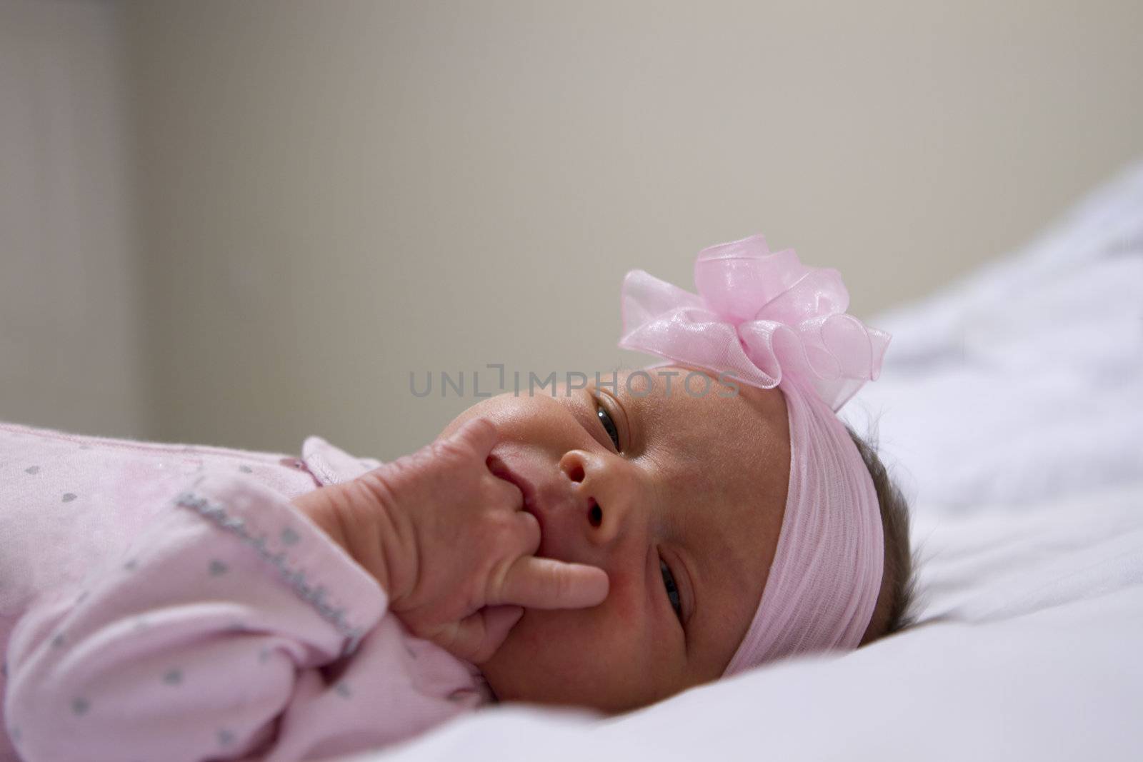 2 days old baby girl sucking her crumply hands while loong at camera with her pink headband.