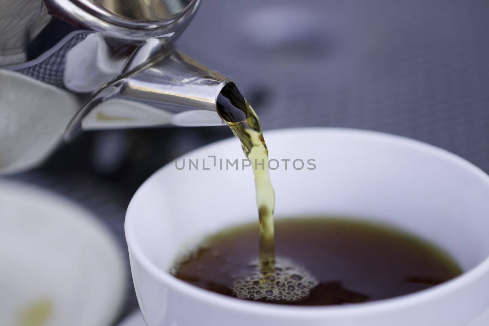 Pouring hot black tea from restaurant style cattle. Selective focused on kettle and poured tea.