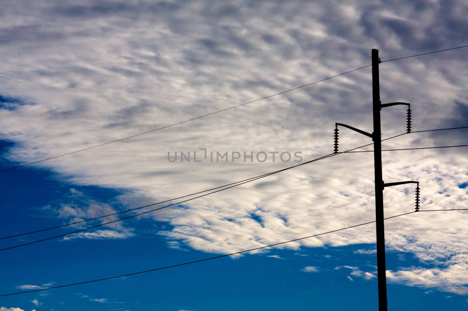 A powerline pole is silhouetted in front of a cloudy sky