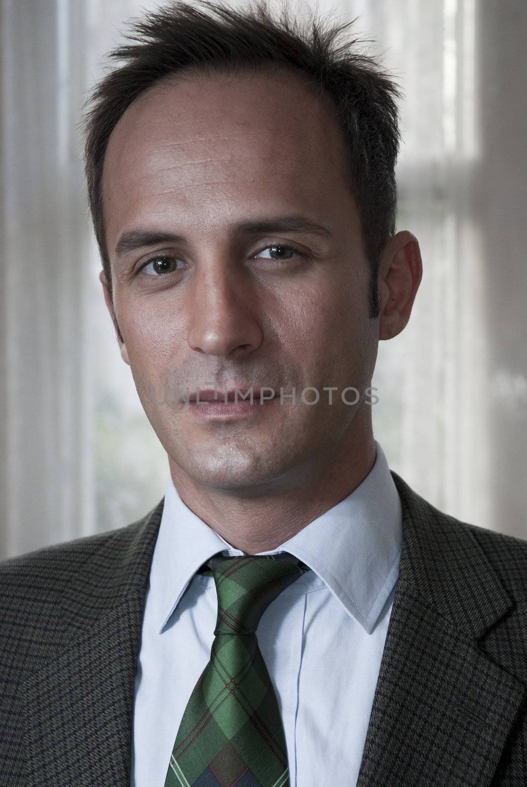 Headshot of white man in a suit with blurred curtain in the background.