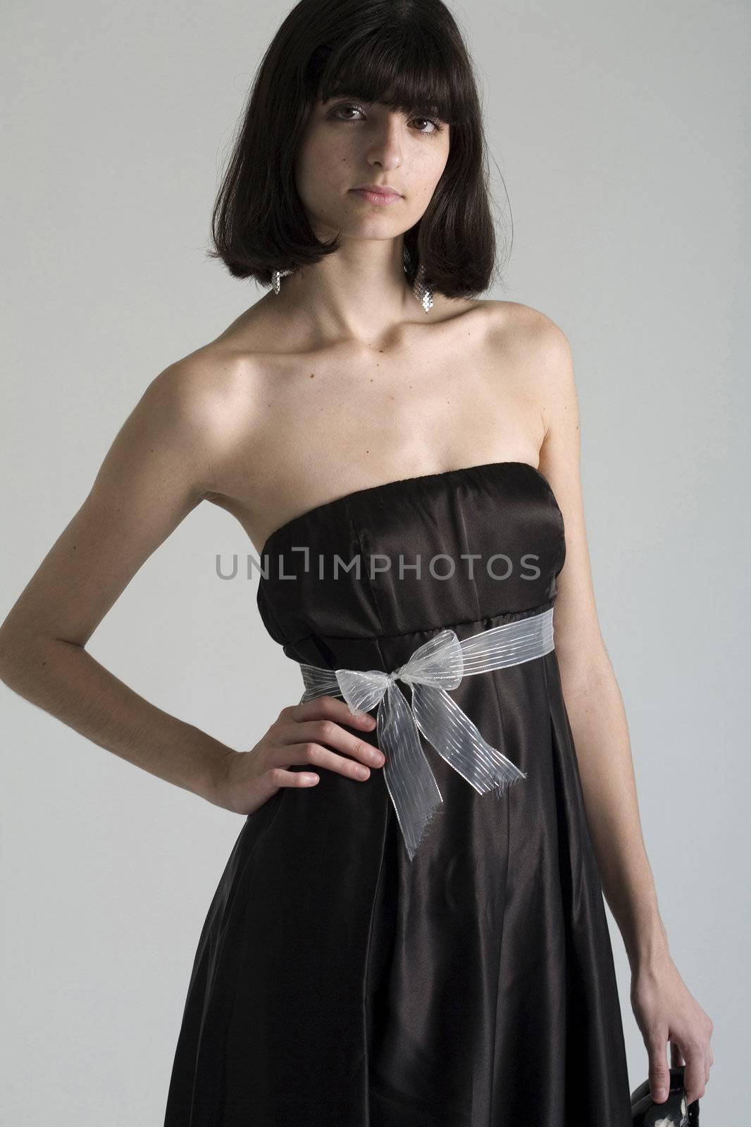 An 18 year old exotic brazilian model, with short dark hair, a young looking face and a skinny body. This was shot in a studio and she's weariing a black, strapless dress holding her shoes.