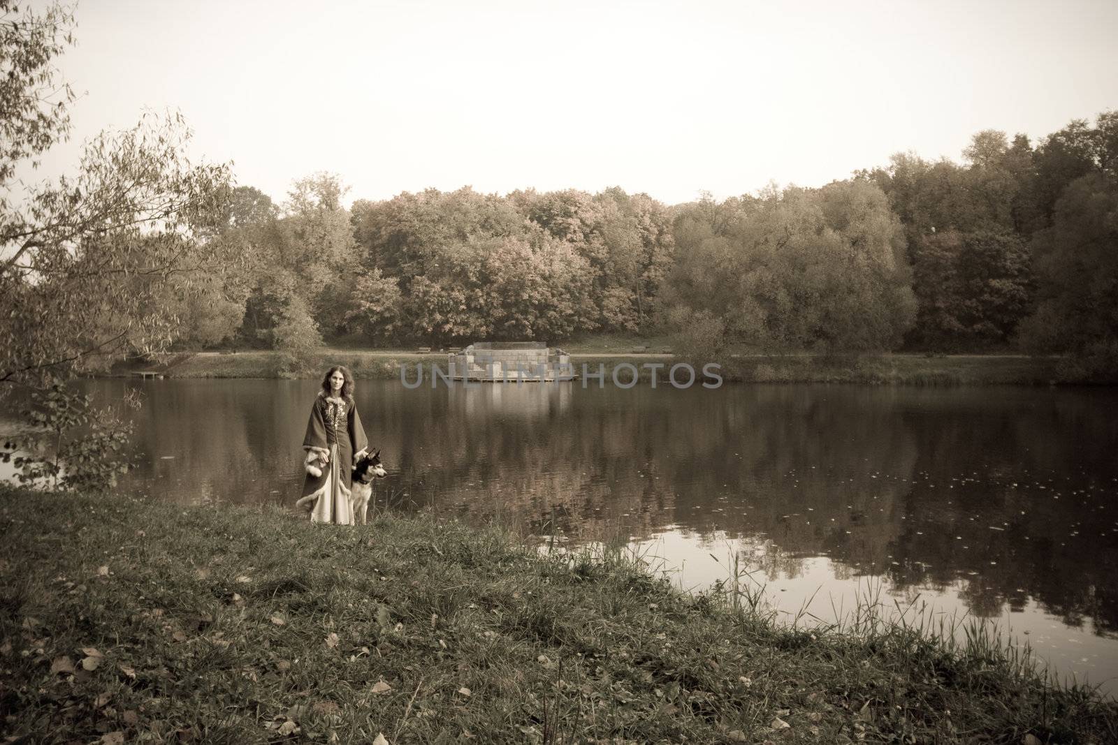 Lady in medieval dress and dog in the forest near river
