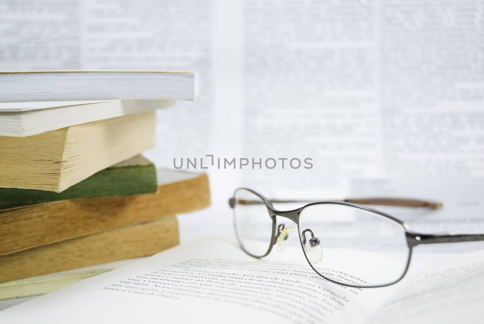 Detail shot of a pair of glasses with stack of books. Blurred letters in the background.
