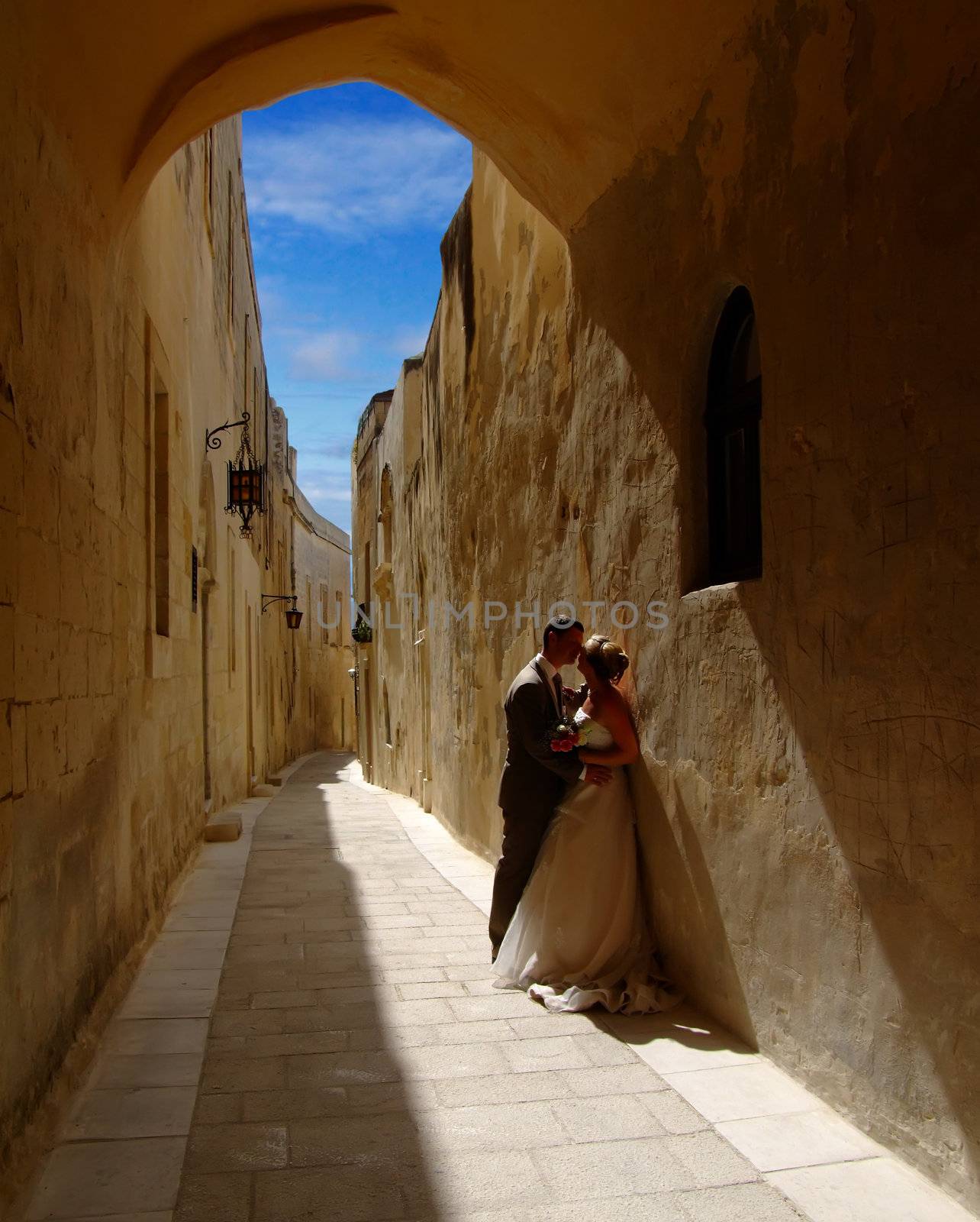 Newsly weds kissing underneath medieval archway in Malta