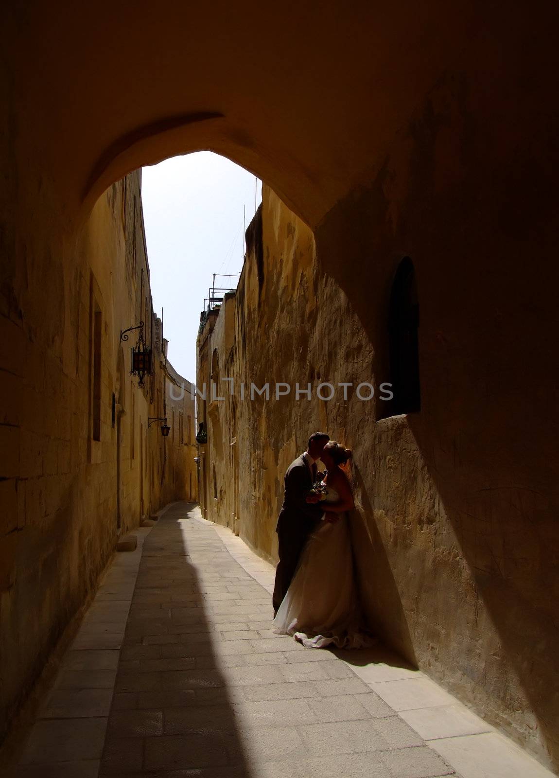 Newly weds kissing underneath medieval archway in Malta, in the setting sun