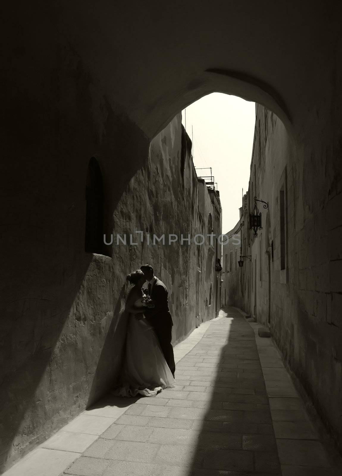 Newly weds kissing underneath medieval archway in Malta, in the setting sun