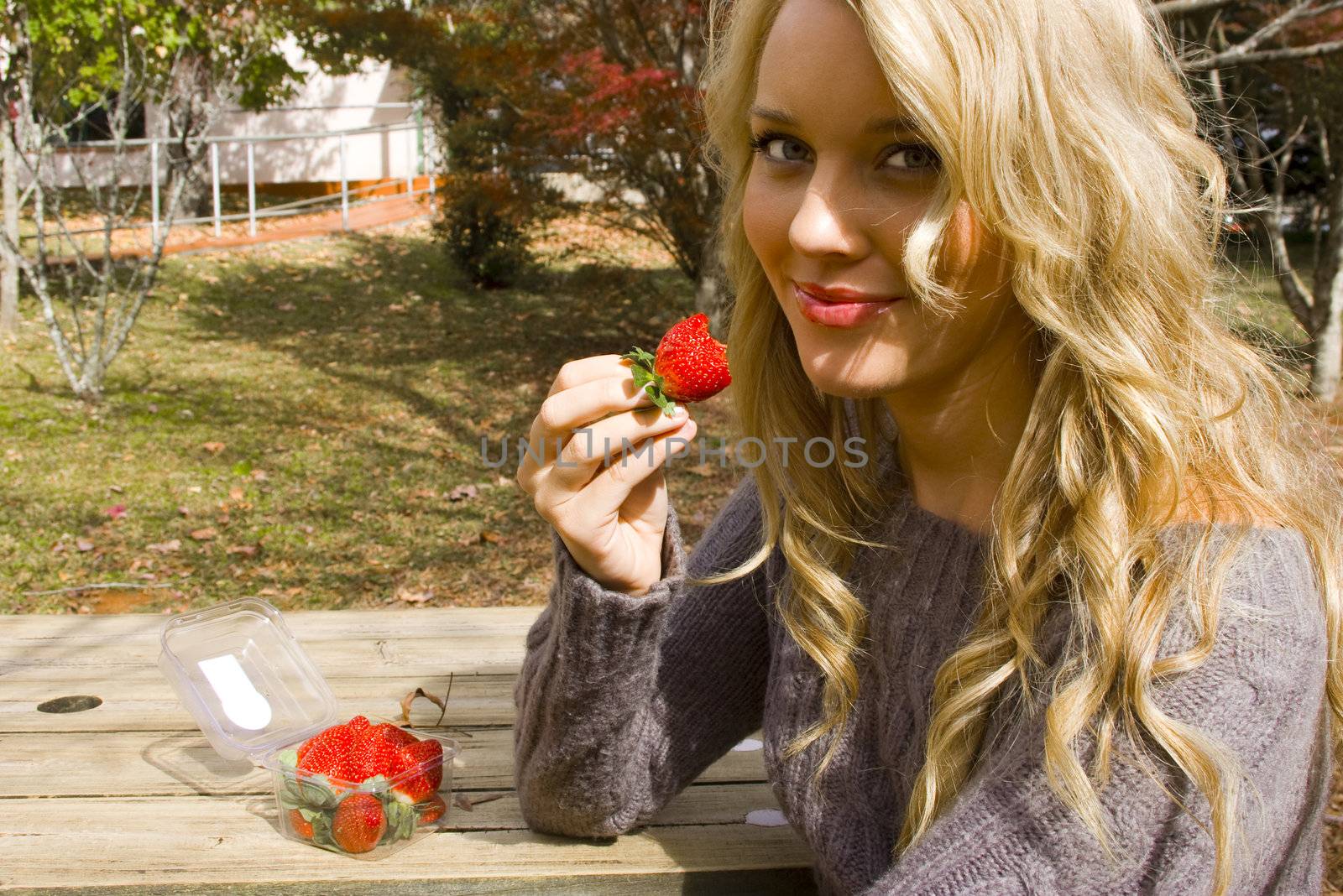 She is eating strawberries outdoors at a park table