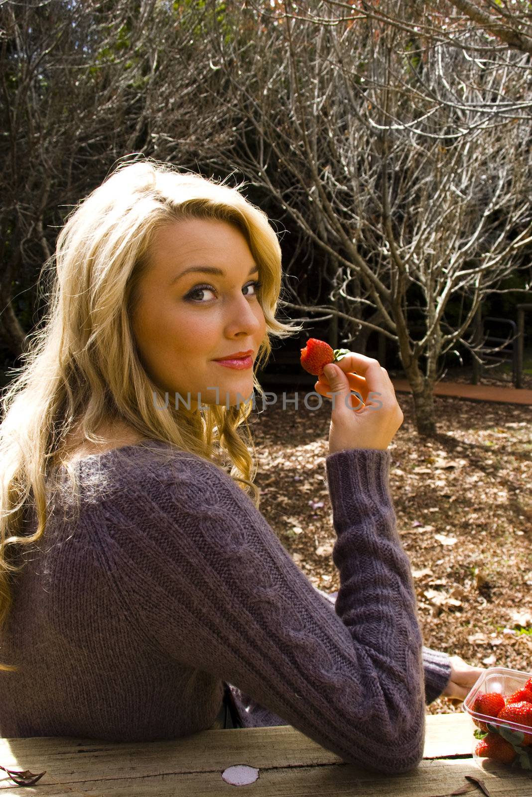Beautiful young woman eating strawberries in the park, looking over her shoulder