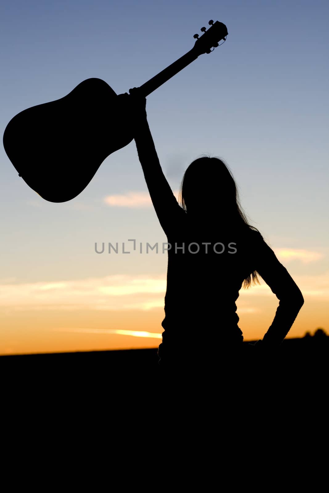 Silhouette of a woman raising her guitar high in the air in confidence or success.