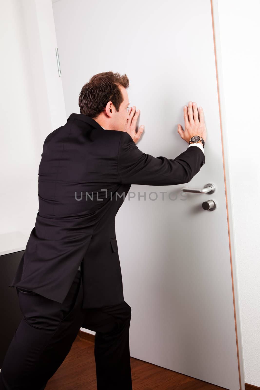 Businessman pushing the door to prevent people entering room
