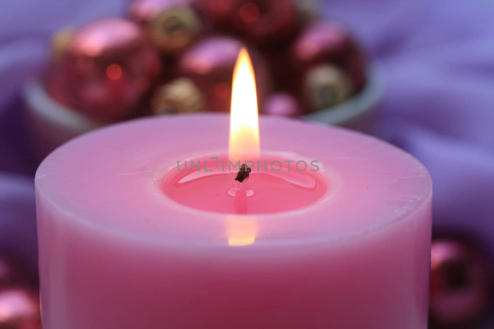 Pink candle with pink christmas decorations on background