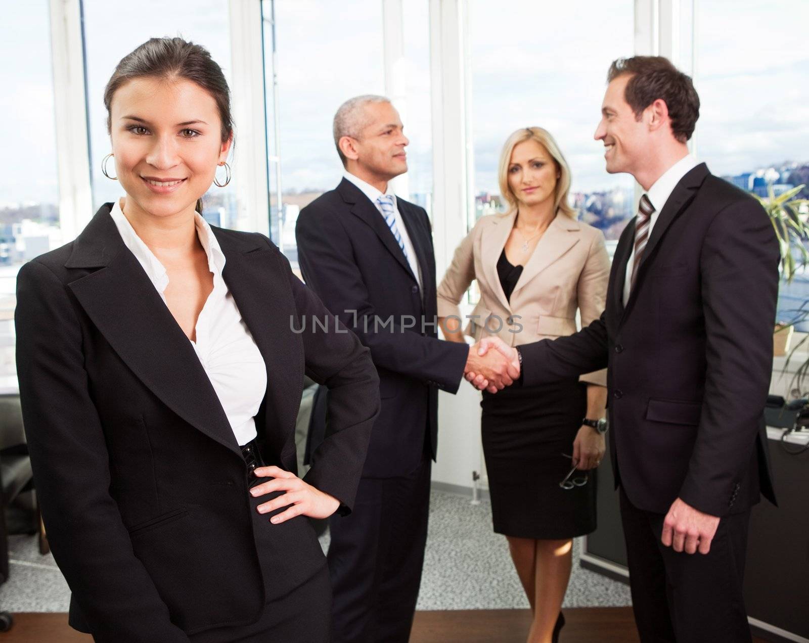Businesswoman sitting in front. Three business colleagues making agreement in background.
