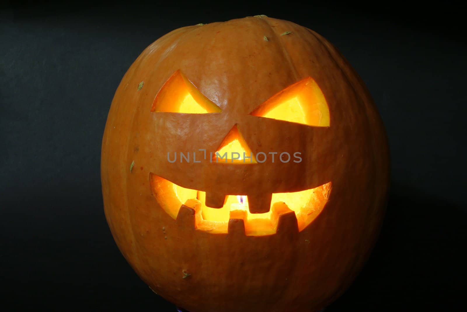 face of halloween pumpkin on black background with candle inside