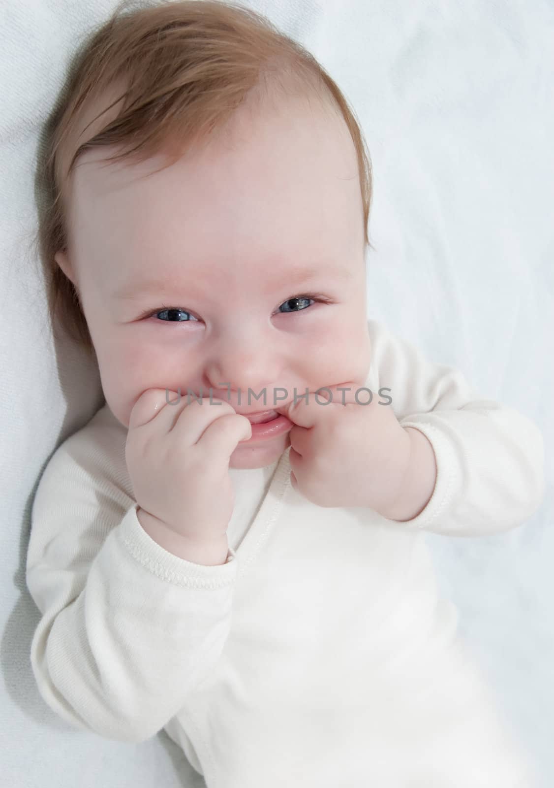 Adorable laughing baby boy lying with hands in his mouth