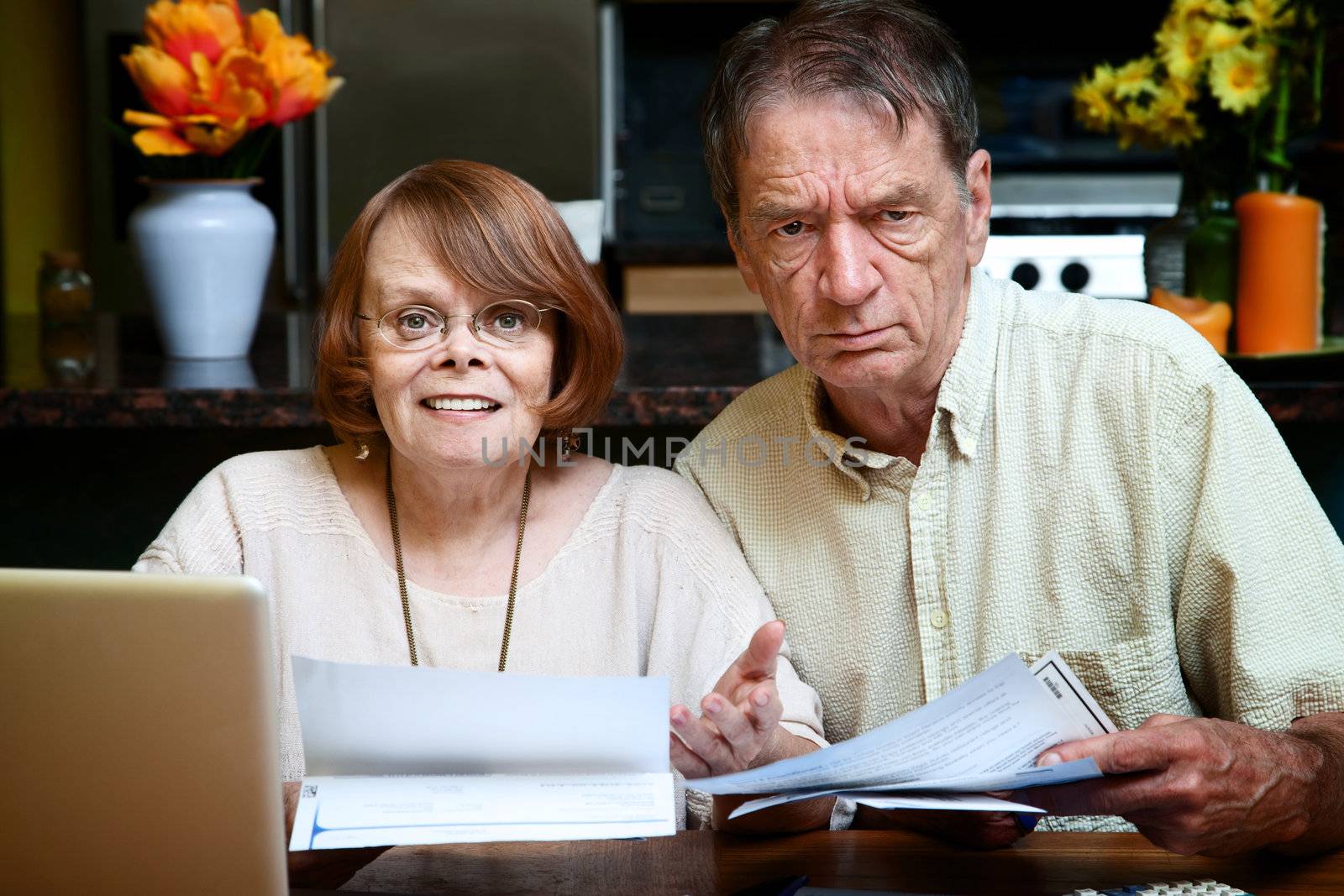 Senior couple at home reacting to many bills