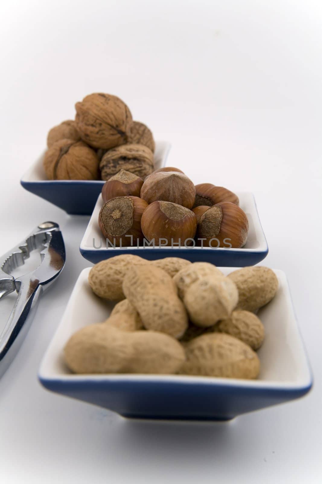 walnuts, hazelnuts and peanuts in three bowls on white background