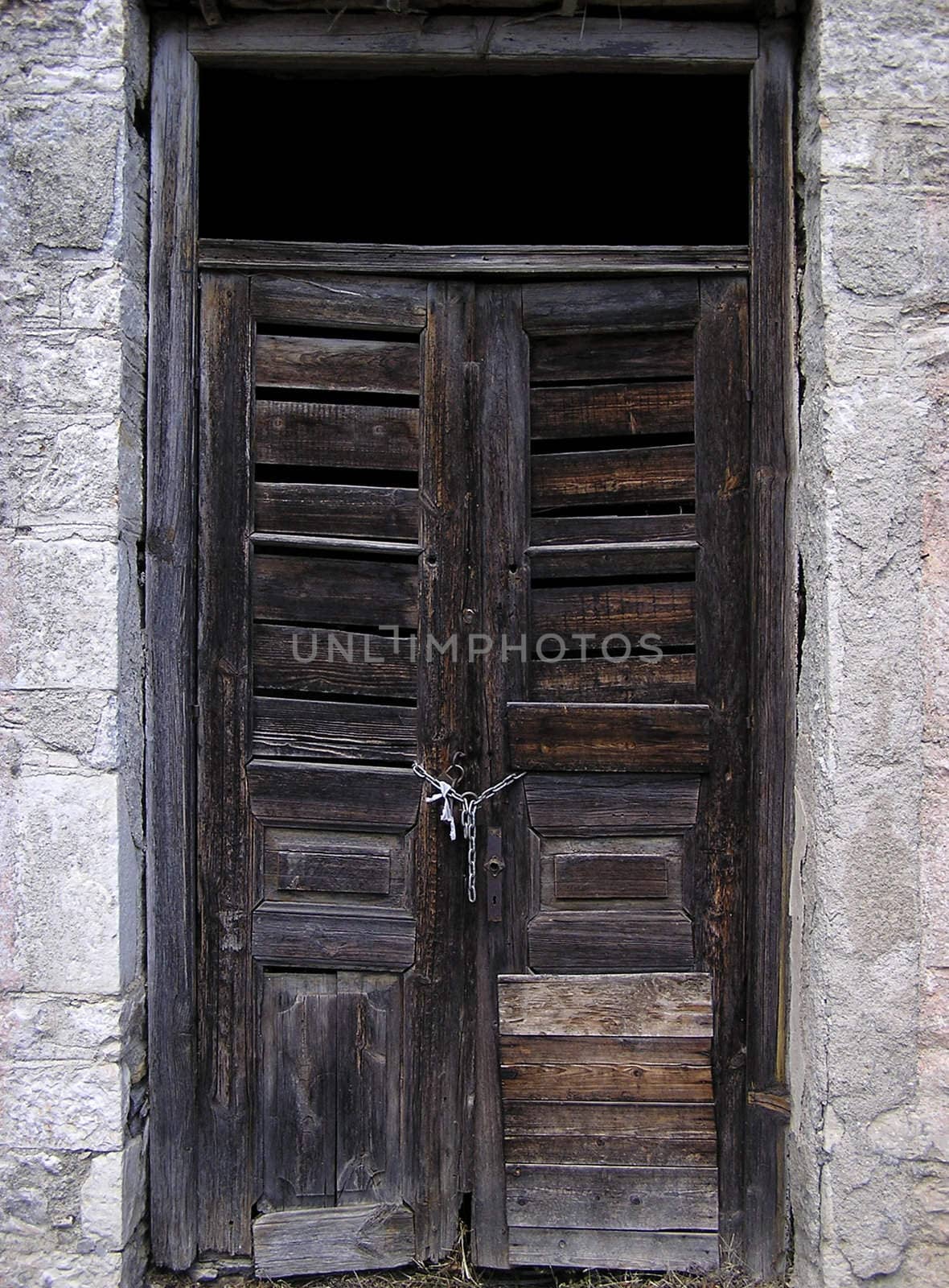 Old ruined door secured by chain and lock.