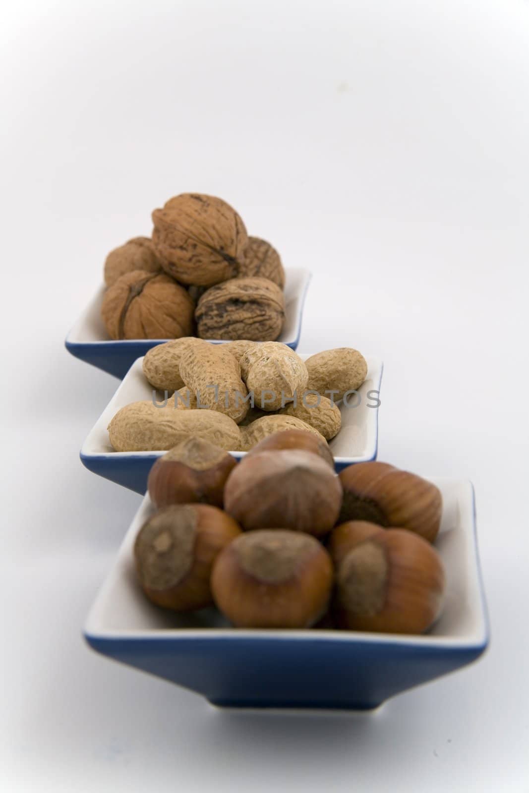walnuts, hazelnuts and peanuts in three bowls on white background