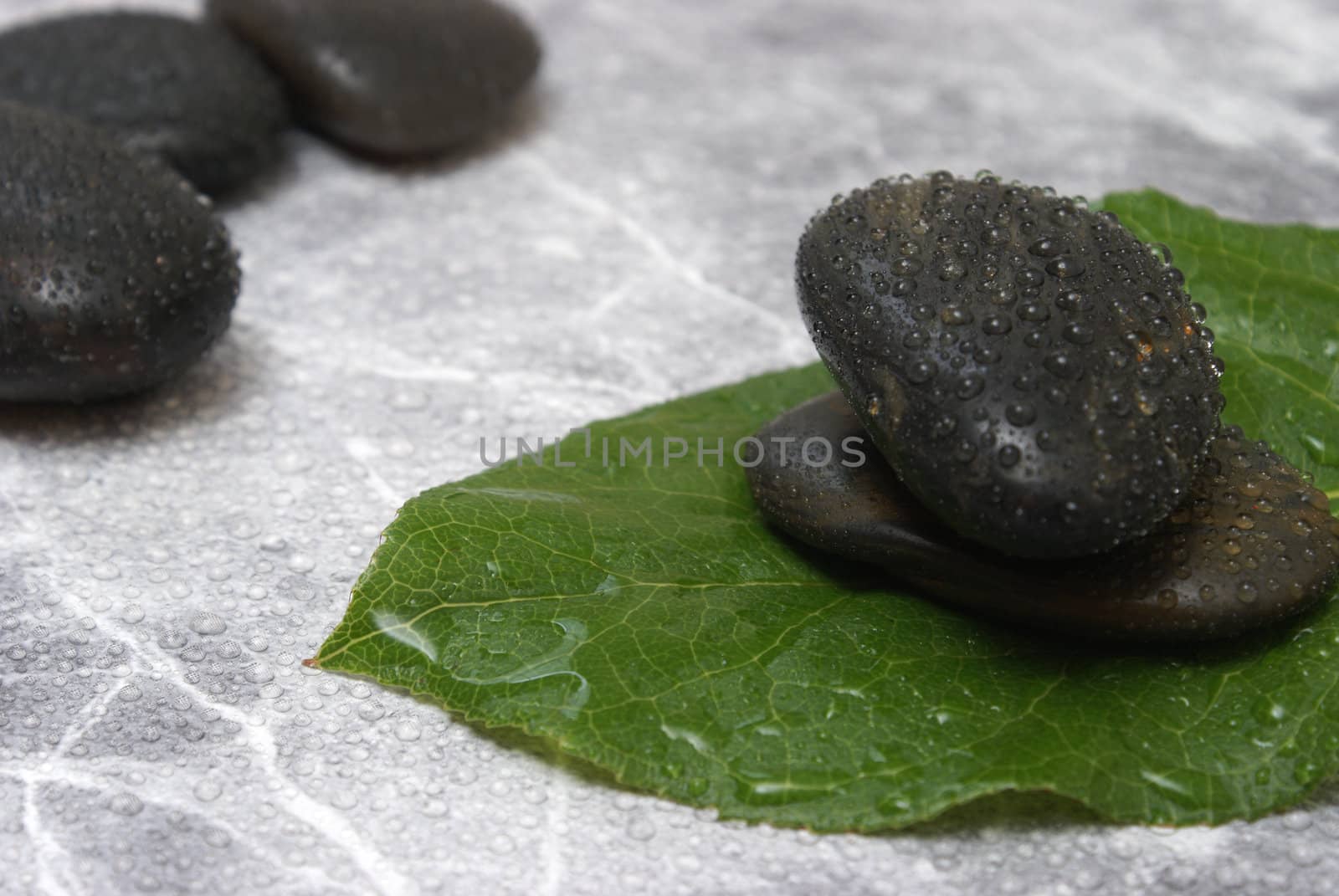 Some fresh water sprinkled over some stones and a leaf which is on a marble background.