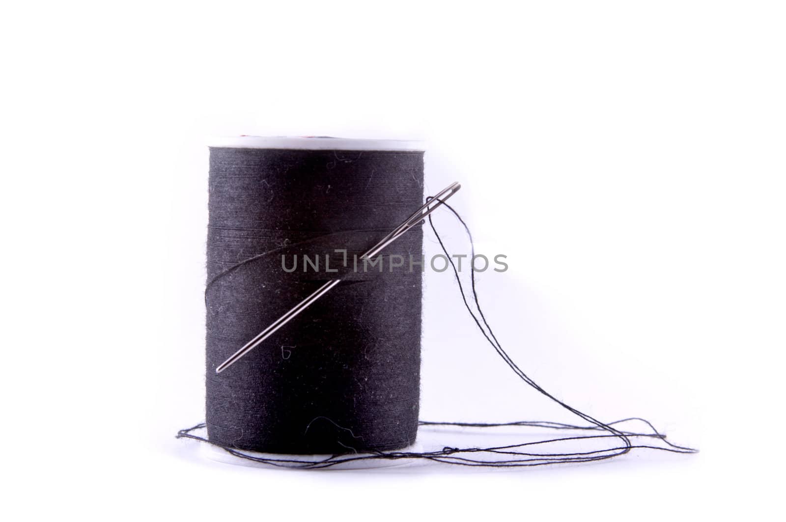 A sewing needle with a spool of black thread, isolated on black