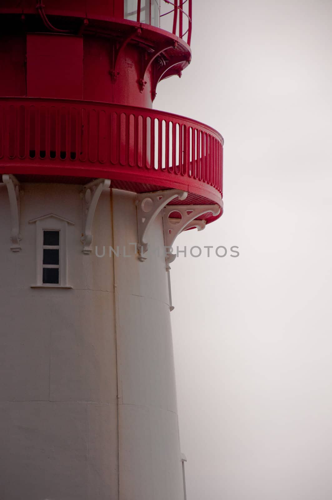 Cropped lighthouse with red details with white sky