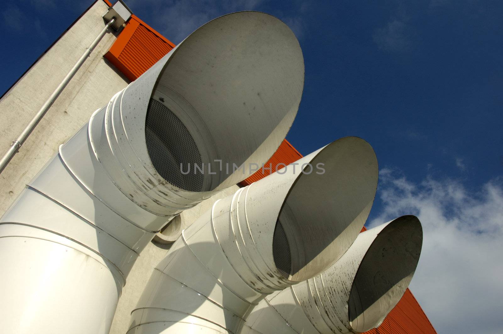 Three industrial ventilation pipes loom large against a blue sky.