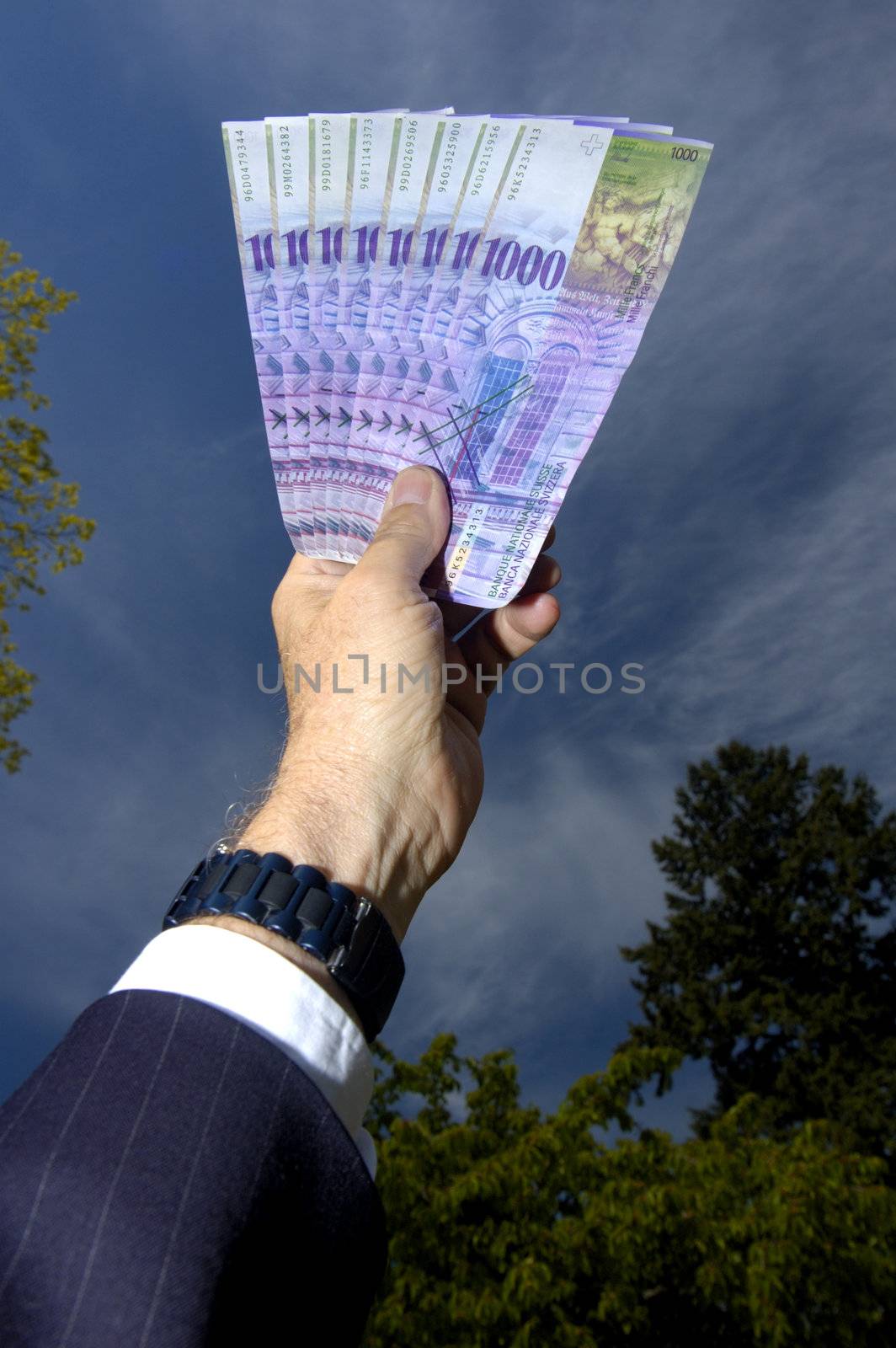 A businessman's hand, holding up 8'000 Swiss francs to the sky.