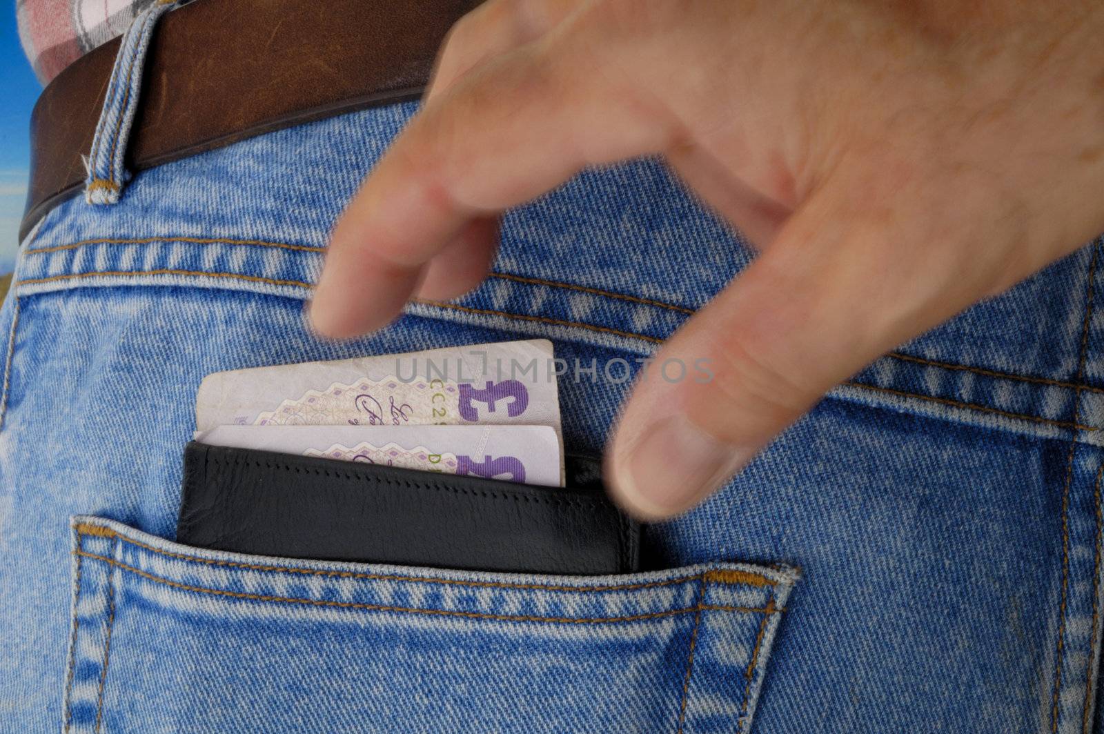 A wallet with two 20 pound notes pokes out of the rear pocket of a traveller's jeans. Motion blur on a pickpocket's hand, about to take it.