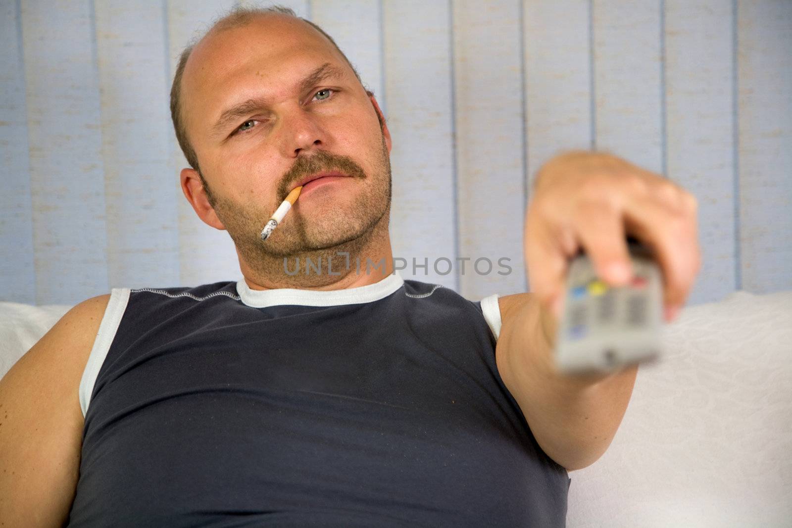 Man sitting on a couch with the remote and a cigarette in his mouth
