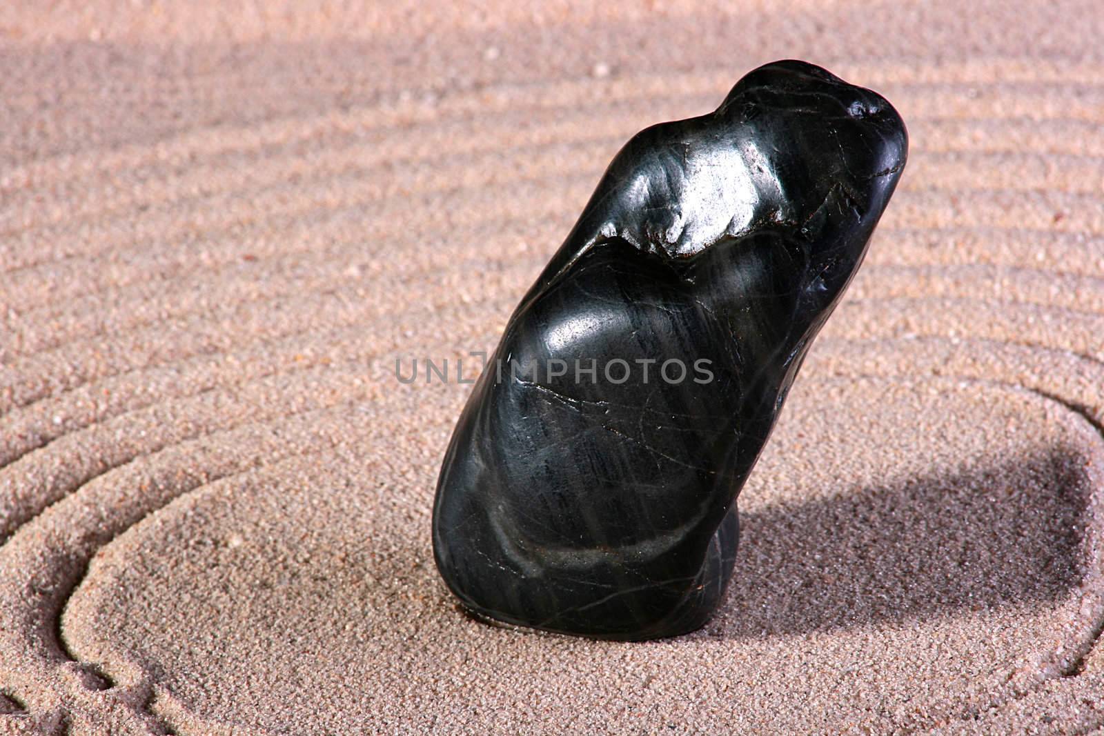 The black stone is on sand with the lined circles round a stone.