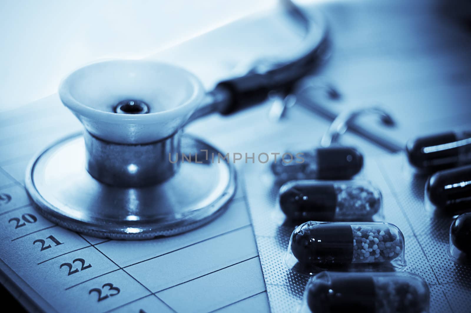 Stethoscope and pills over notebook blue toned