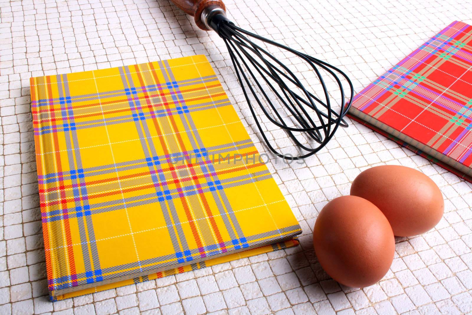 Two books for recipes on a kitchen table with eggs and a beater.