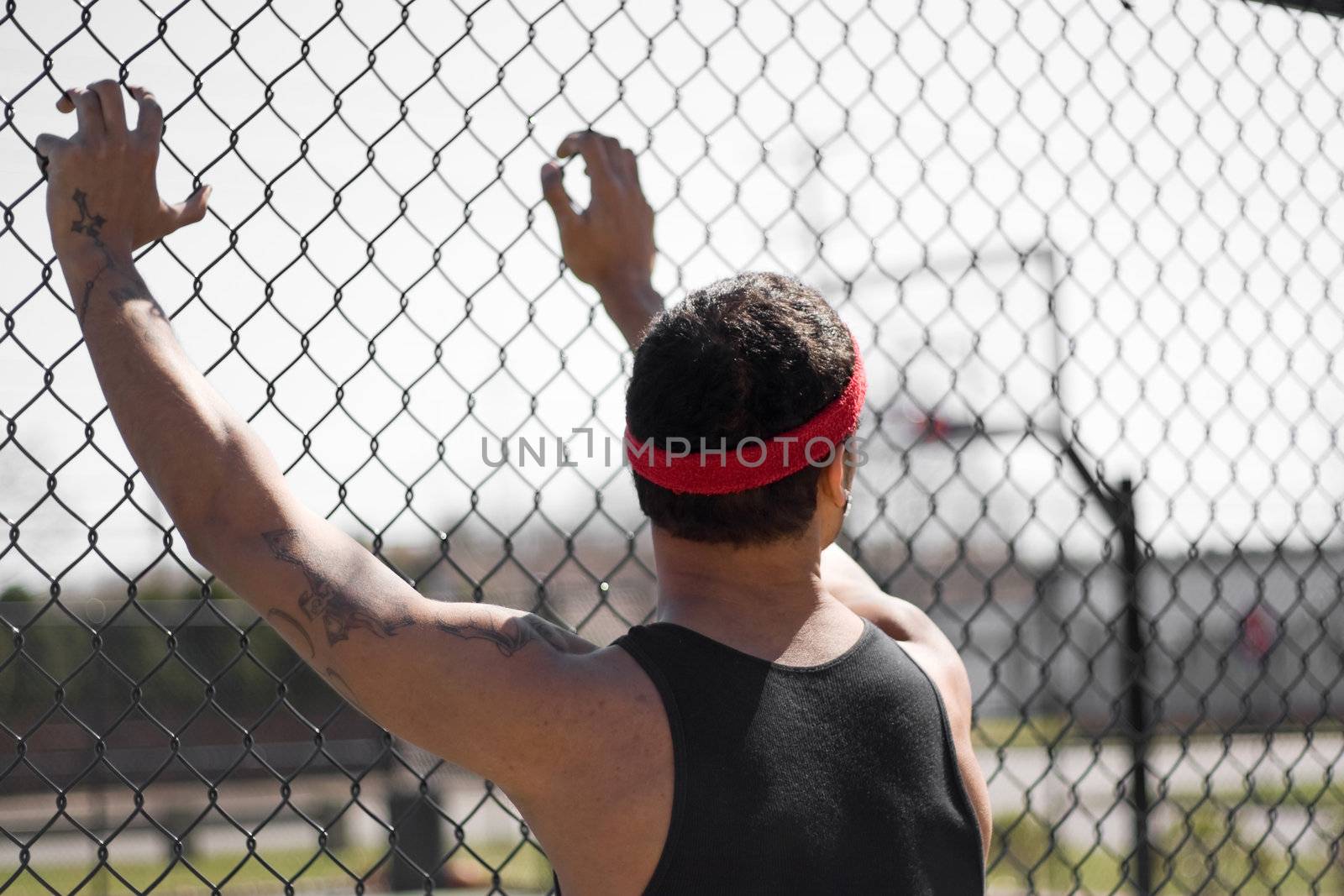 A young basketball leaning up against the chain linked fence at the basketball court.